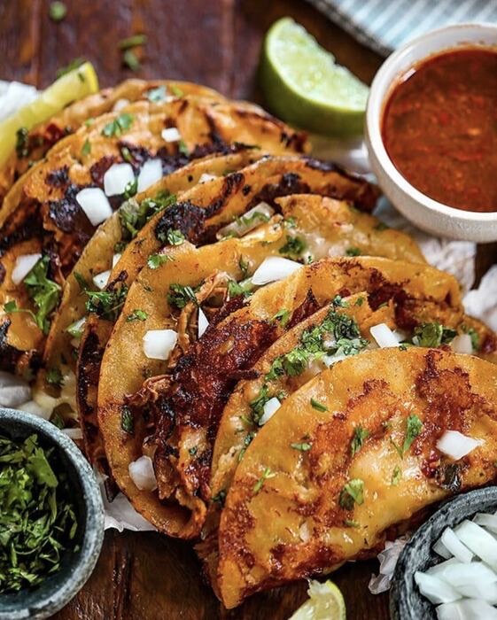 Birria tacos with consommé, lime, cilantro, and onion