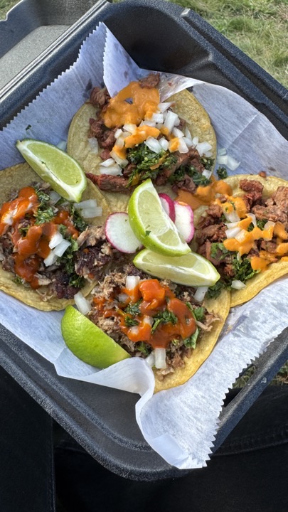 Four Salcido's street tacos in a black takeout tray with lime and radish